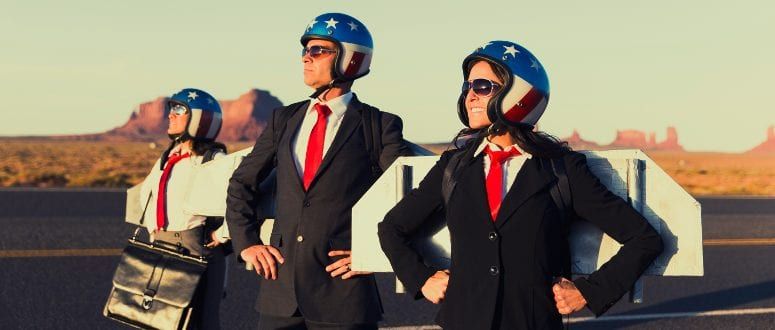 Three people stand with their hands on their hips wearing rocket wings and American flag helmets.