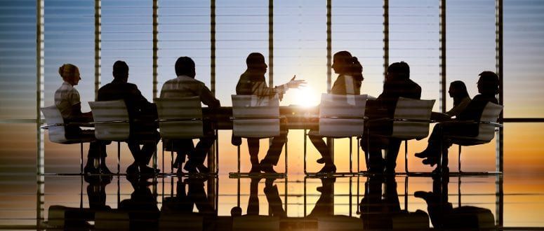 A group of people work around a table in an office at sunset.
