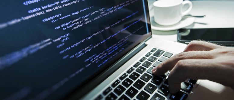 A person works on a laptop. The screen displays code.