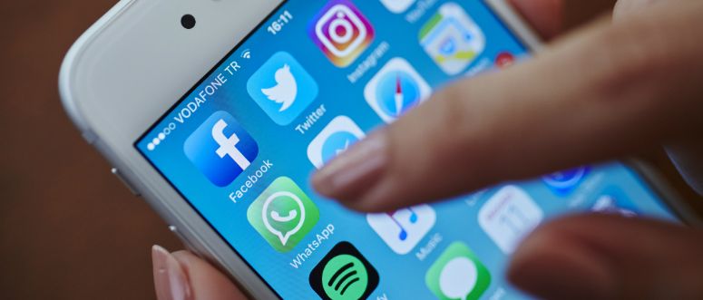 A smartphone displaying social media icons. A person's finger moves towards one of the icons.