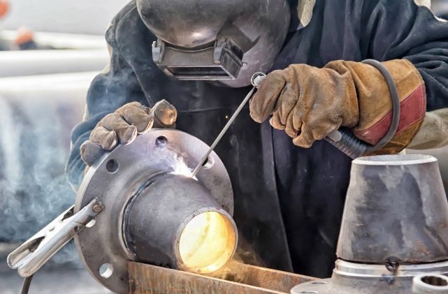 A welder in full P P E welds a piece of metal.