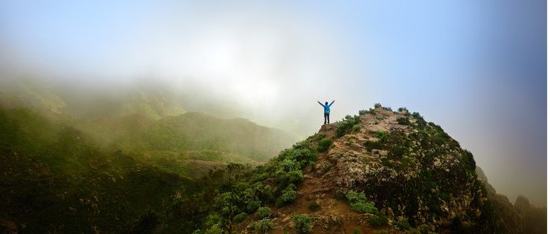 A person near the peak of a mountain raising their hands above their head.