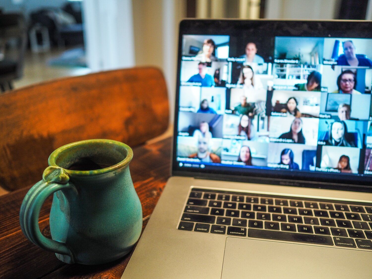 A photograph of an open laptop displaying a video chat with over 20 people. A mug is next to the laptop.